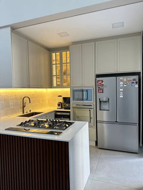 Cozinha cinza com armários de moldura, cristaleira iluminada e ilha com cooktop.