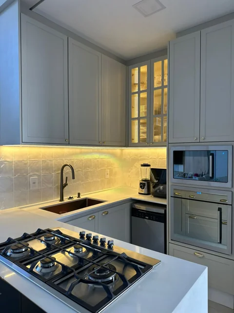 Detalhe da cozinha cinza com portas emolduradas e vidro canelado iluminado.