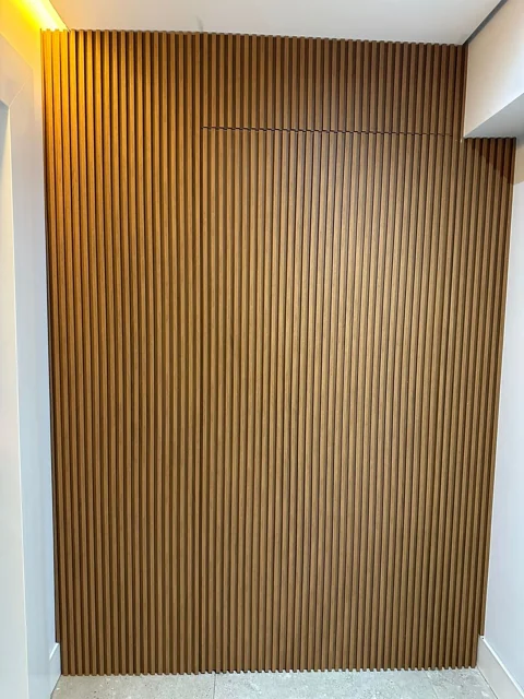 Porta integrada em painel ripado amadeirado, do piso ao teto.